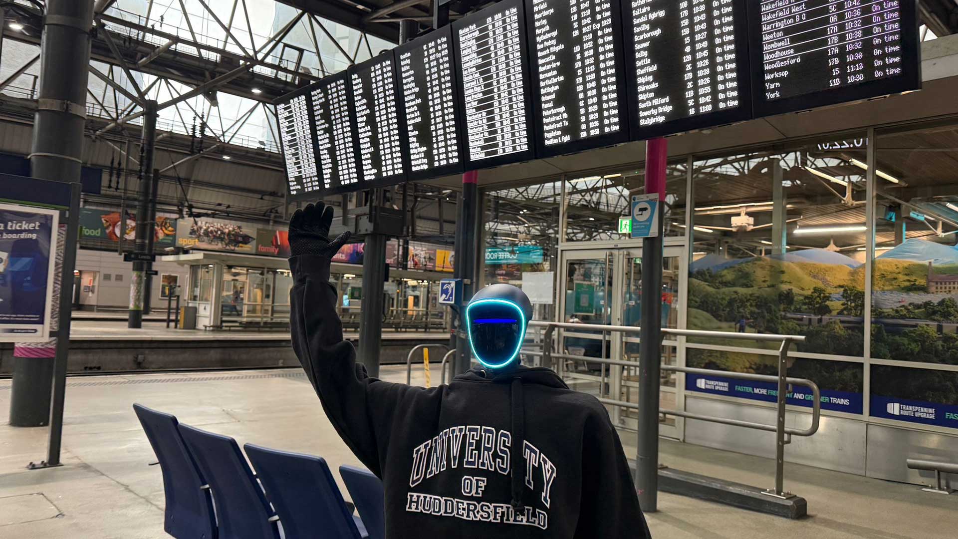A humanoid robot waiting to camera in front of the time table at a train station