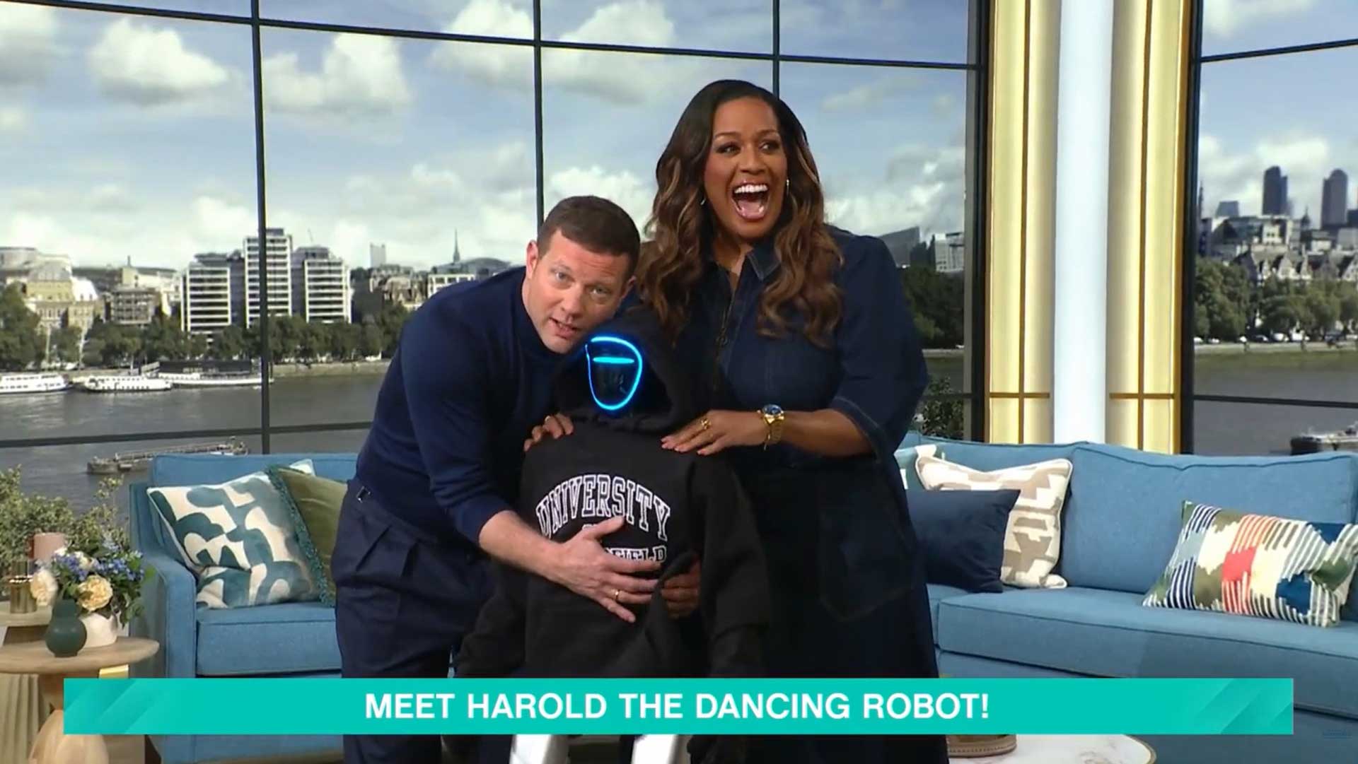 Dermot O'leary cuddling Harold the Robot on the set of This Morning. Alison Hammond smiling giving Harold a shoulder rub.