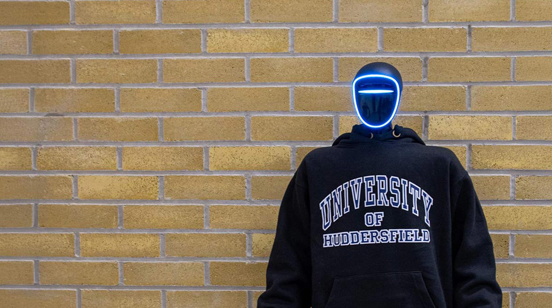 a humanoid robot wearing a hoodie and stood in front of a brick wall