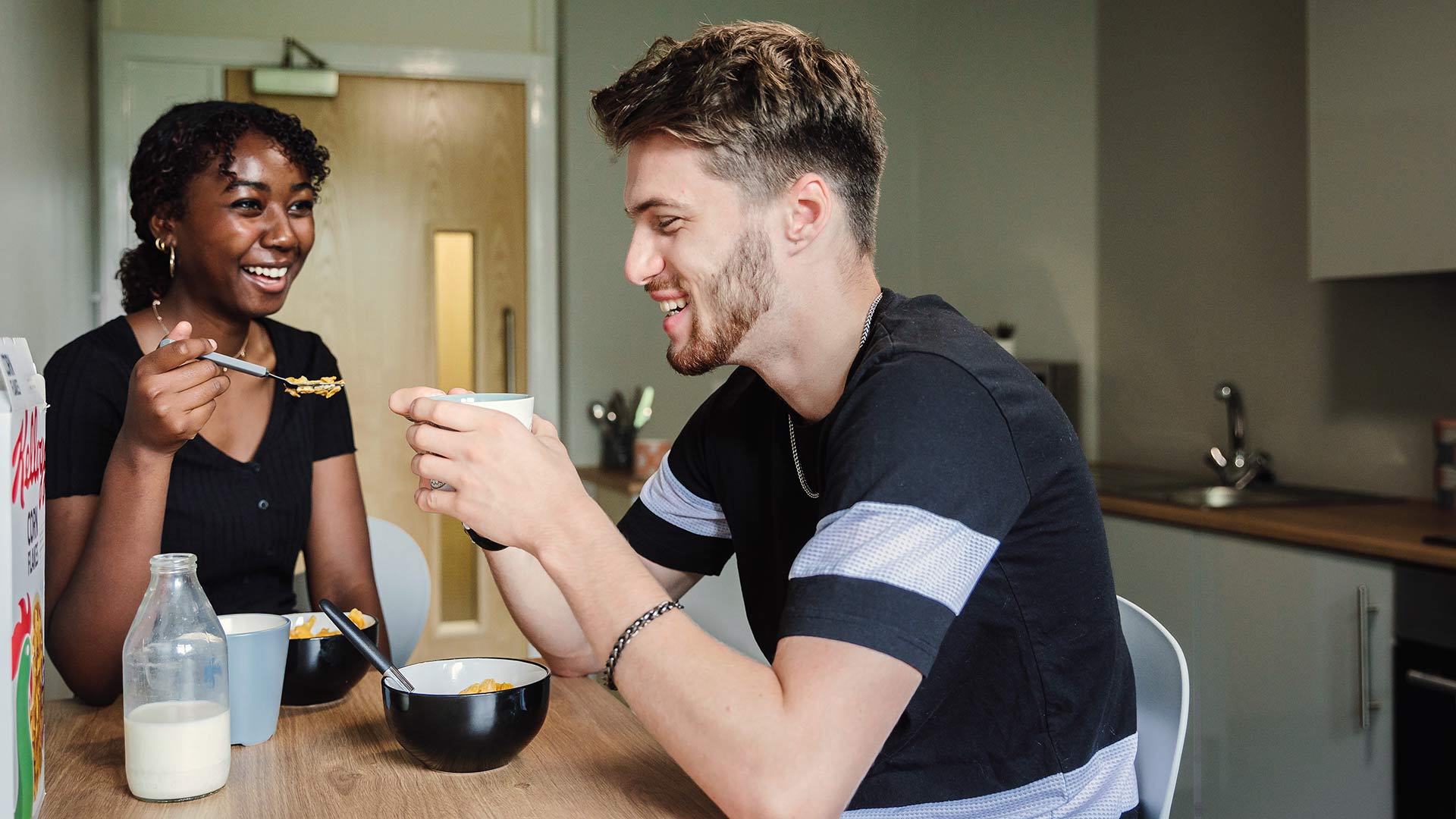 Two students sat together eating breakfast in a kitchen in halls