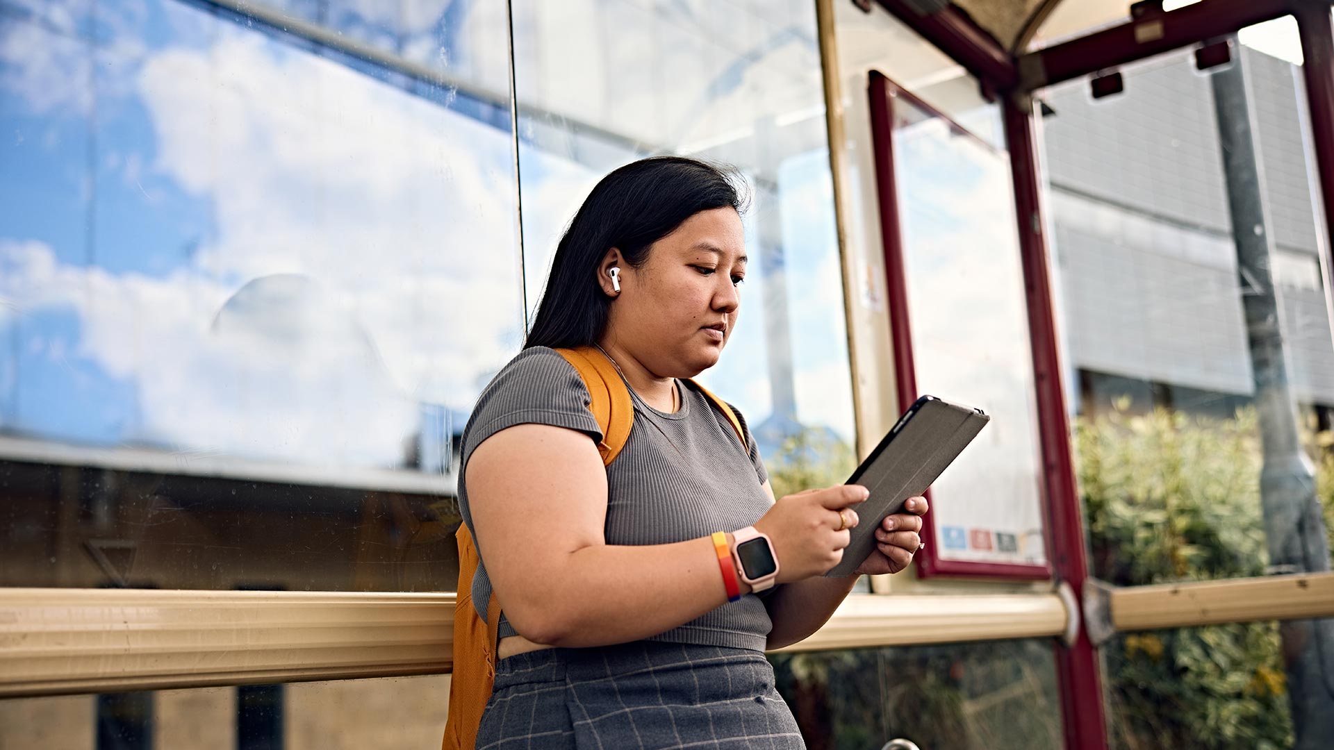 A student sat a bus stop using a tablet device.