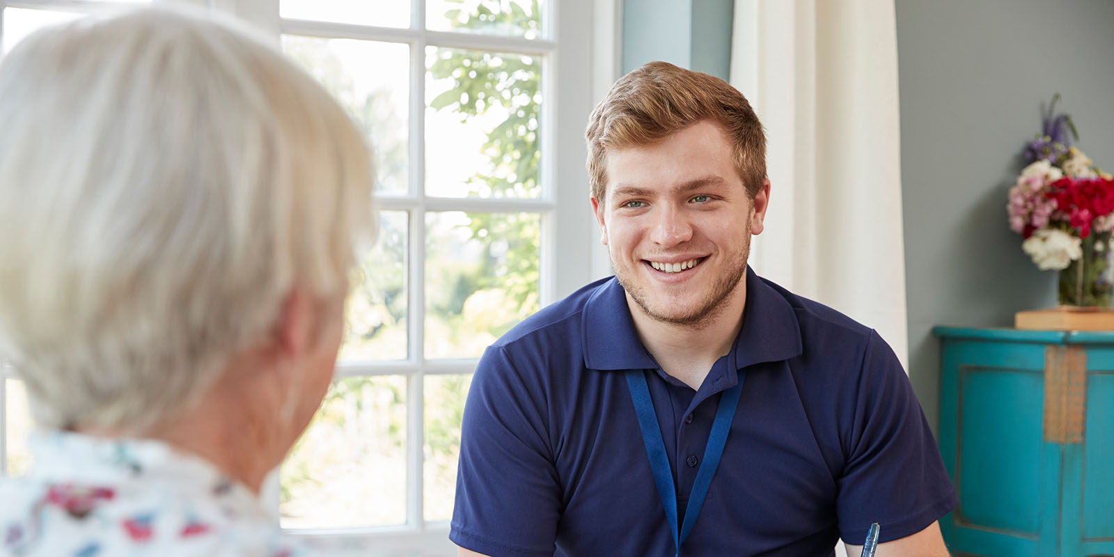A young male nurse smiling at an older woman who is mostly outside the frame