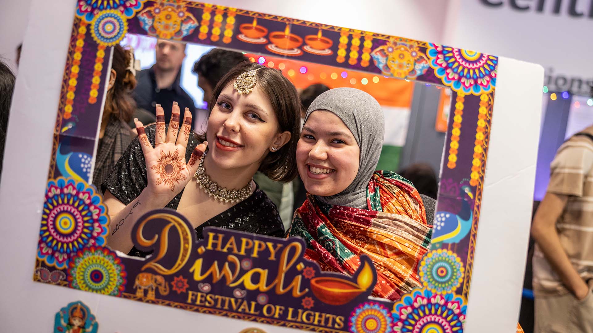 Two students smiling at the camera holding a Diwali sign