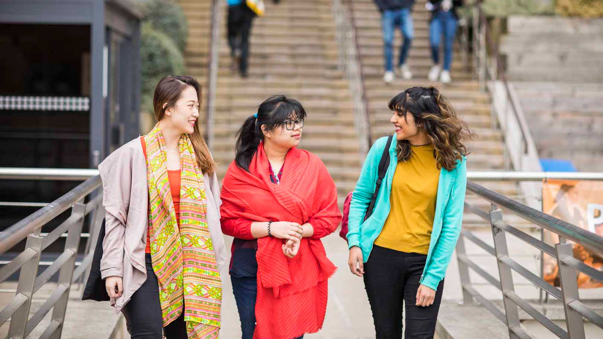 An image with three international students walking across a bridge.