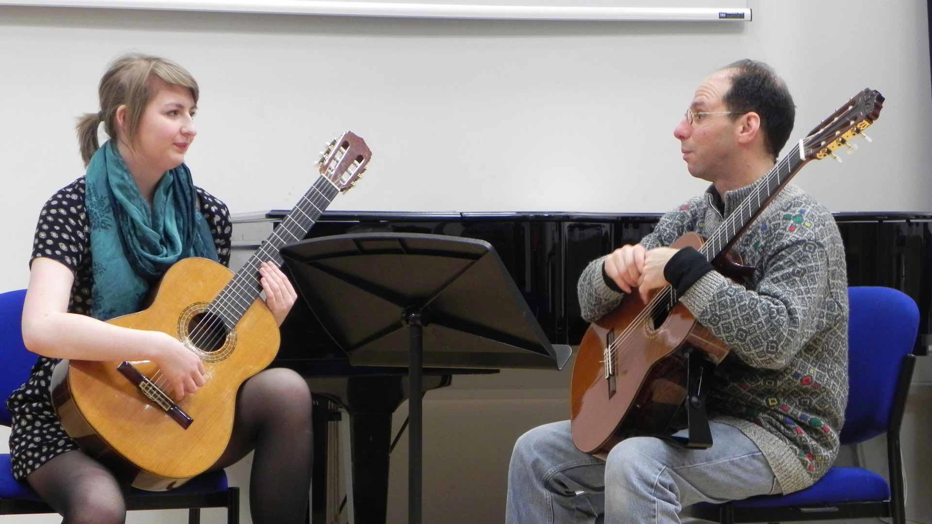 A student learning to play the guitar with an instructor