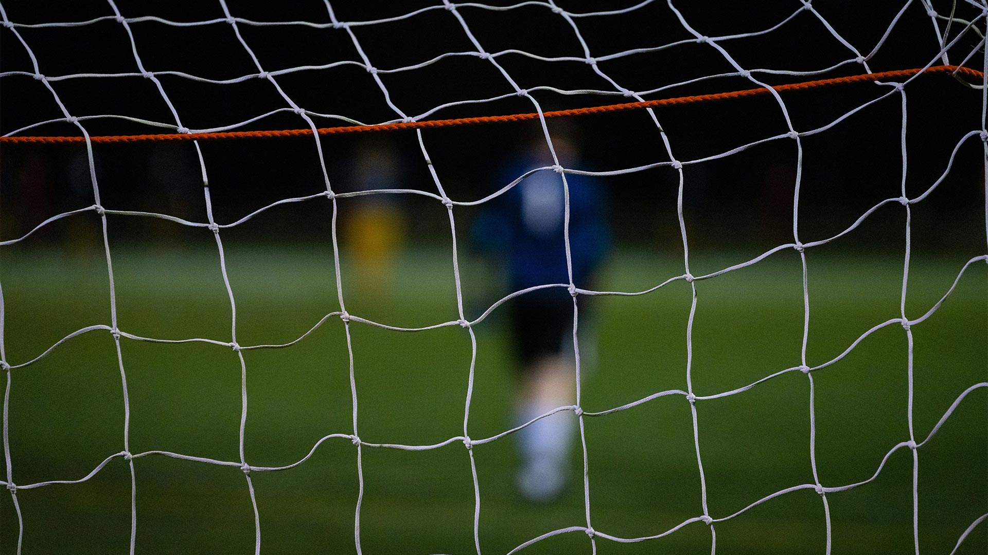 A football player on pitch seen through the goal net