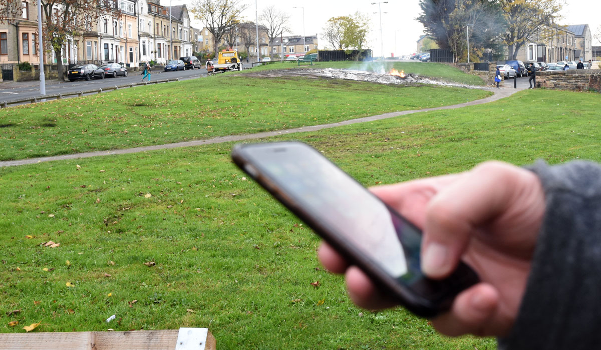 holding a mobile phone with a fire in the background