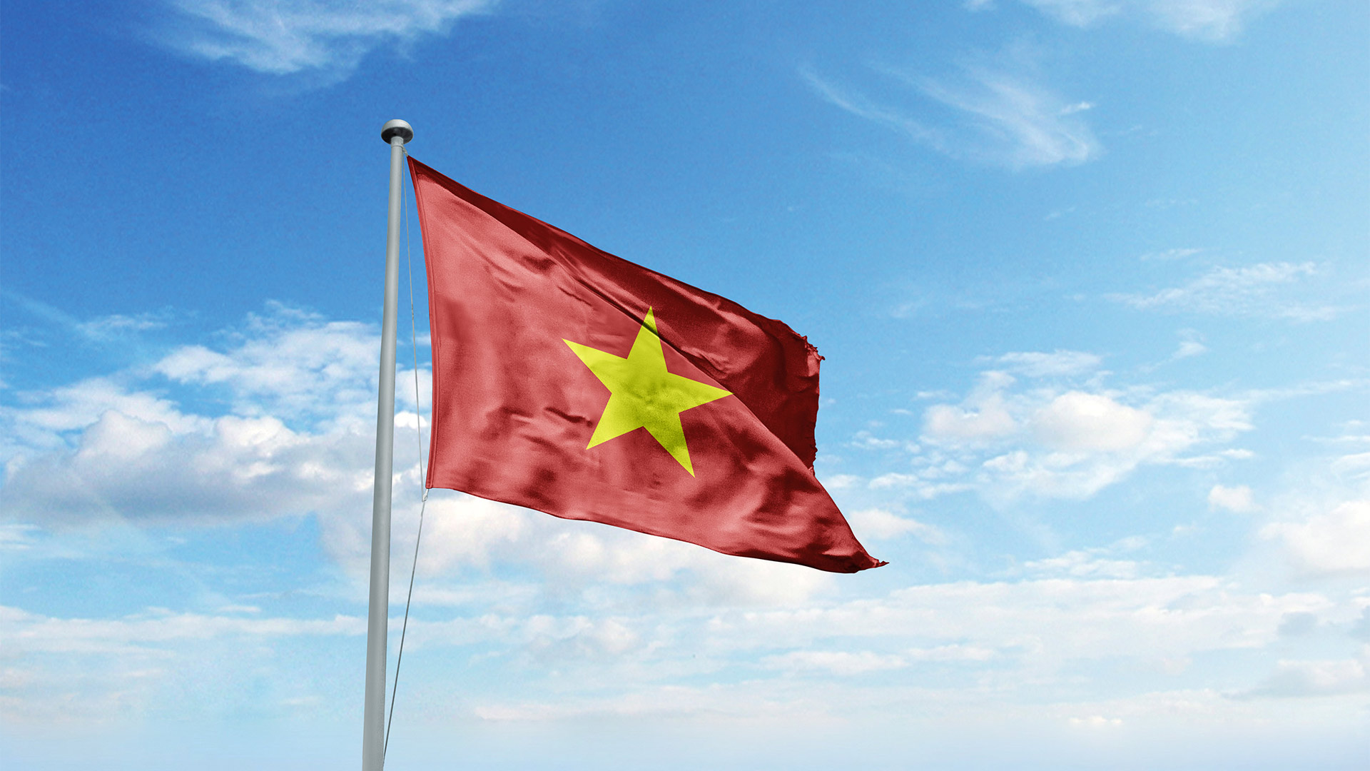 The flag of Vietnam on a pole with a blue sky in the background