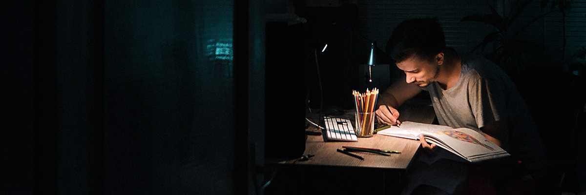 A student studying in darkness by a lamp