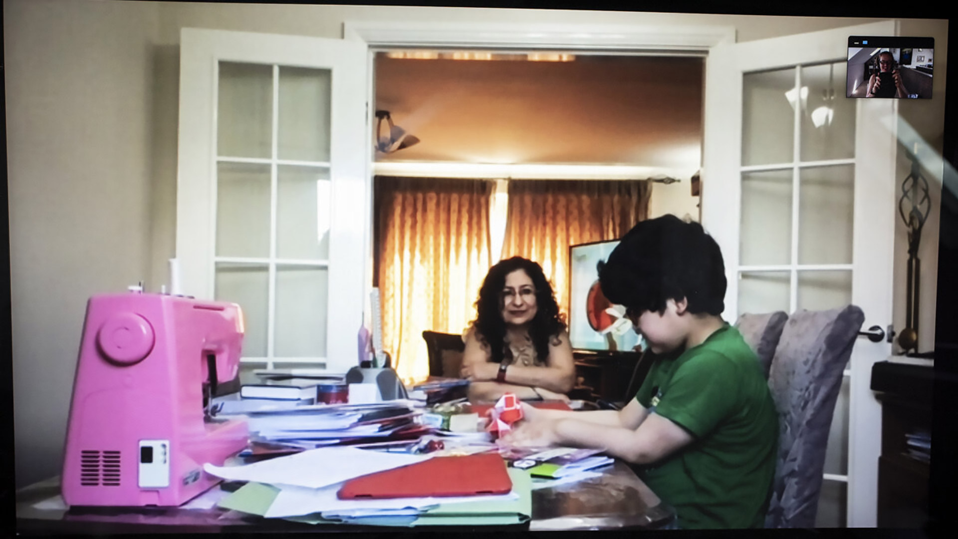 Simmi sits at the dinning table which has become her son’s work desk and is covered with papers and a pink sewing machine.