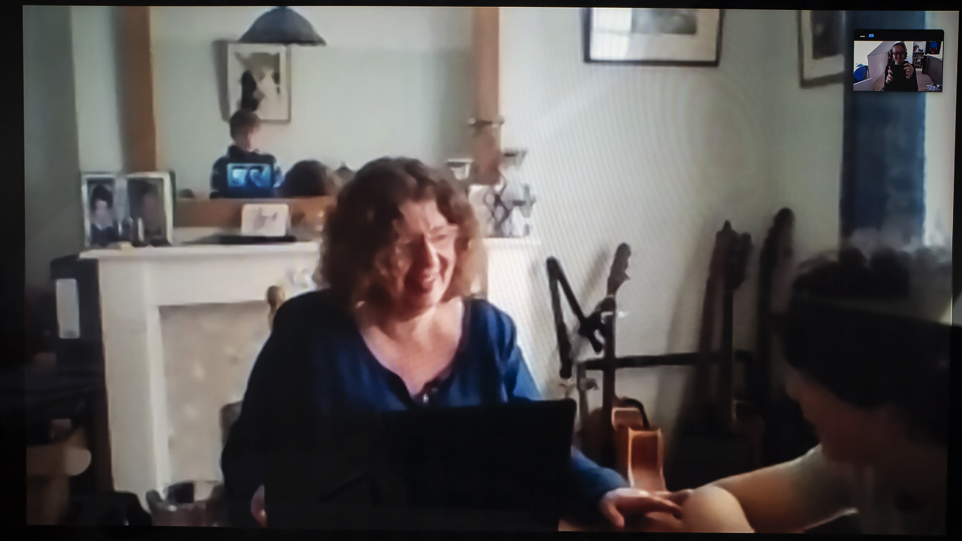 Tracey sitting in front of a fireplace working on a laptop whilst her son asks her a question