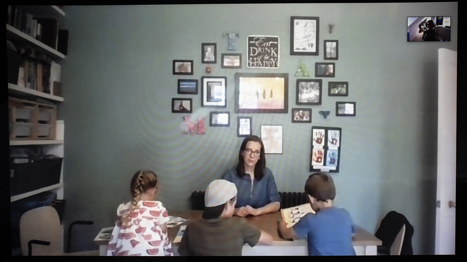 Claire sitting at the kitchen table in front of a gallery wall with her three children. They often work here, captured remotely by photographer Fran Monks.