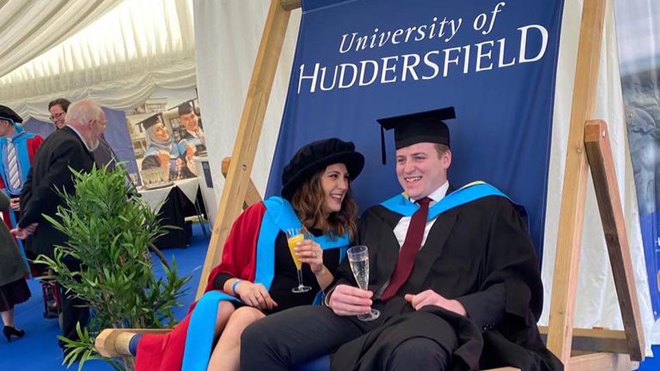 Dr Grace Parfitt and James Linsley sat in their graduation garb in an outsize deckchair