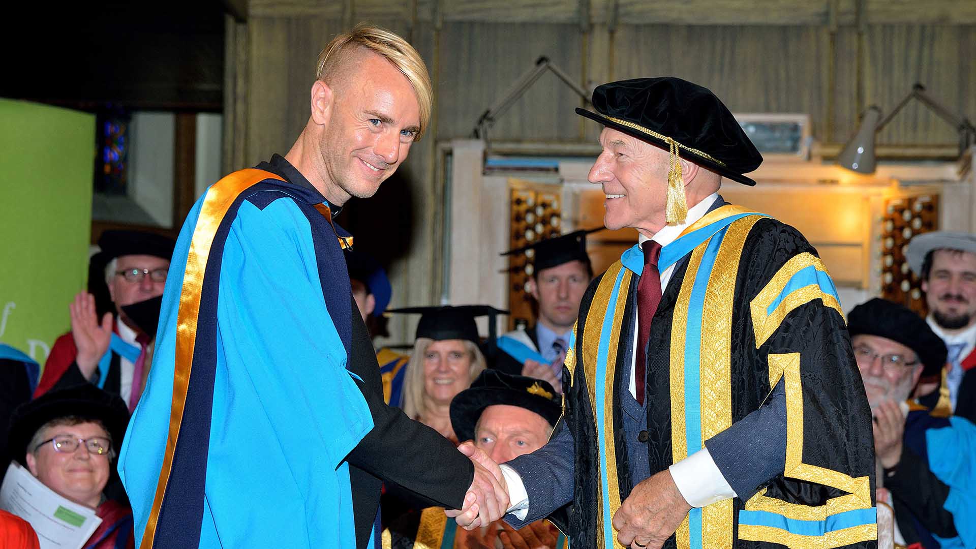 Richie Hawtin shakes hands with Sir Patrick Stewart while wearing honorary graduation garb