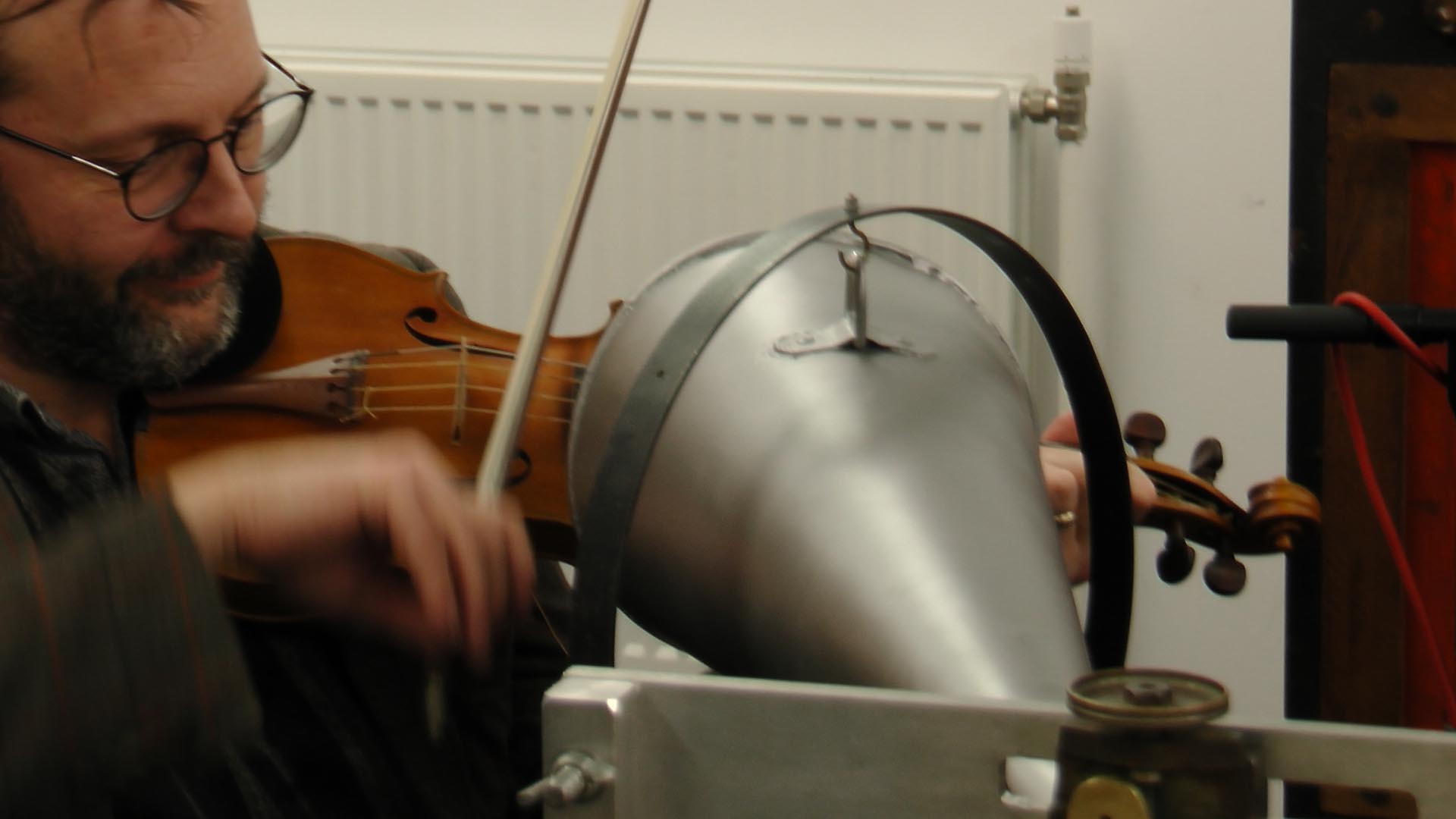 David Milsom plays a violin close to an old piece of recording technology