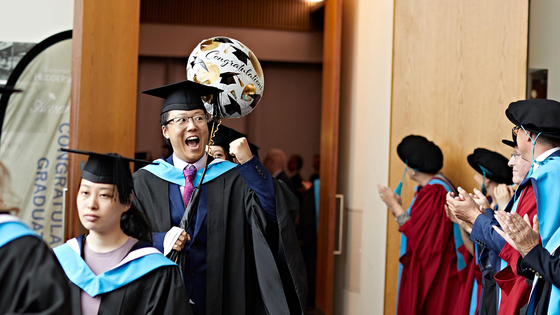 A student celebrates getting his degree by smiling and waving a lot