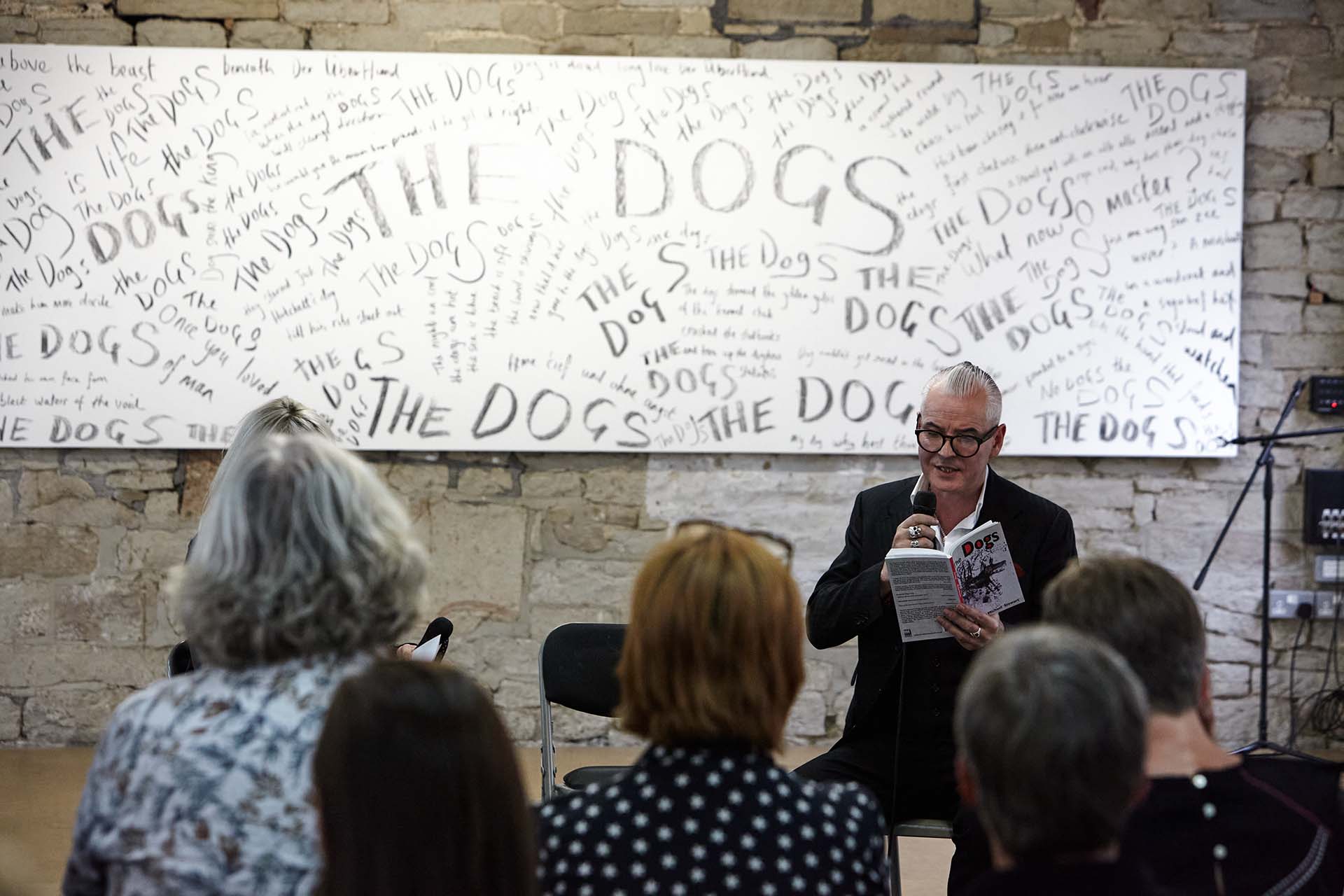 Dr Michael Stewart sat in a room reading from his book The Dogs