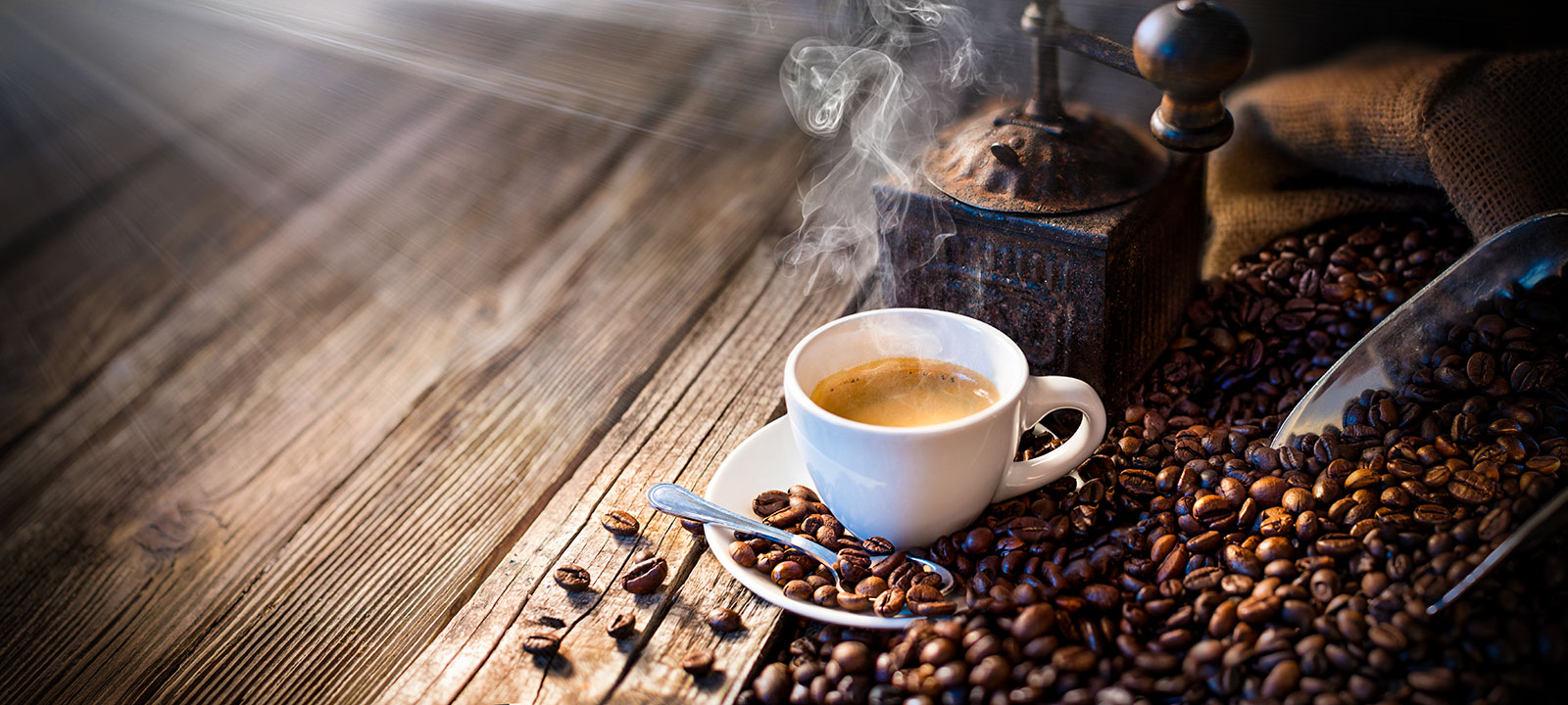 A cup of espresso sat ontop of coffee beans in front of a coffee grinder