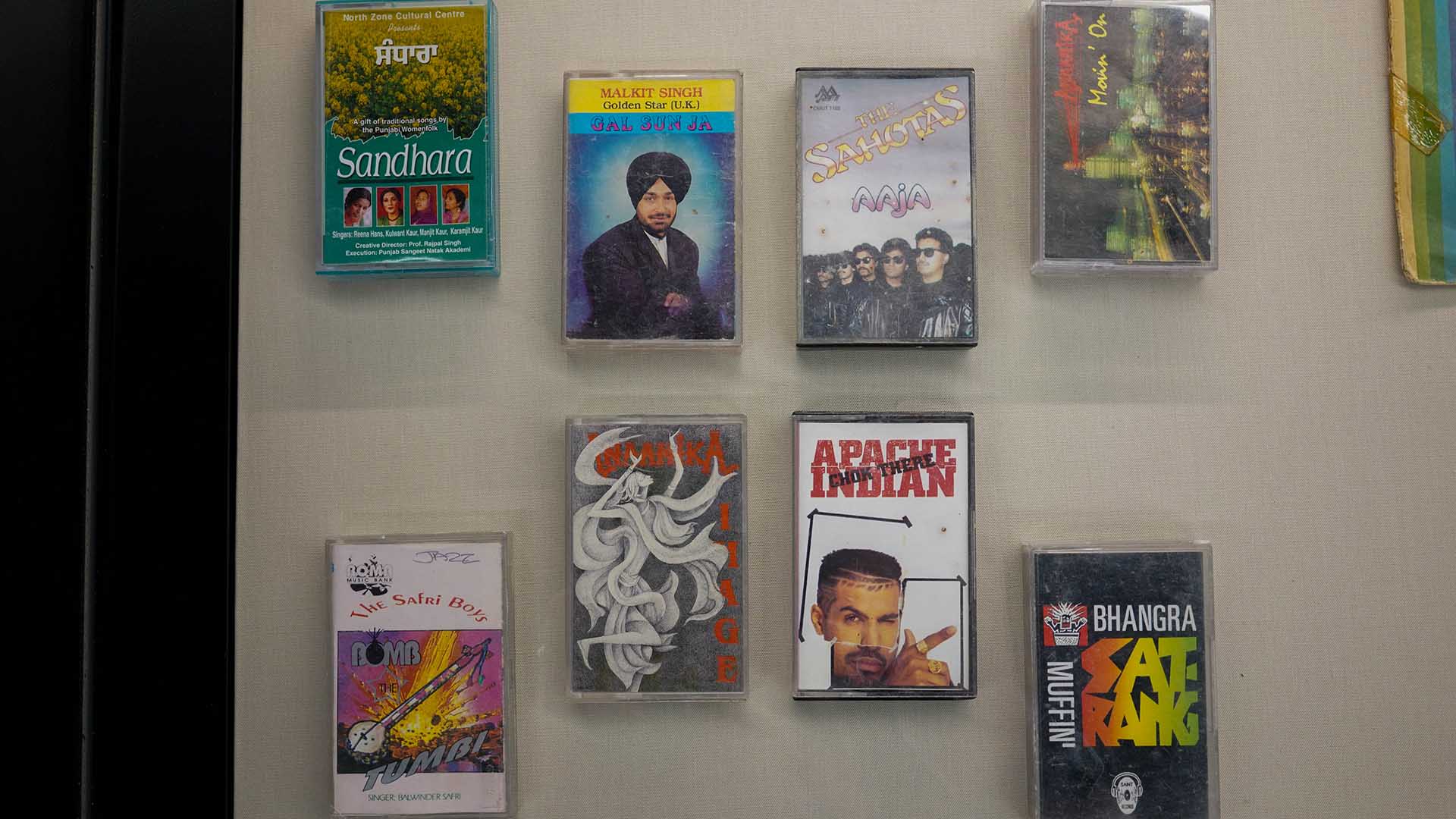 Some cassette tapes of bhangra music in a glass case