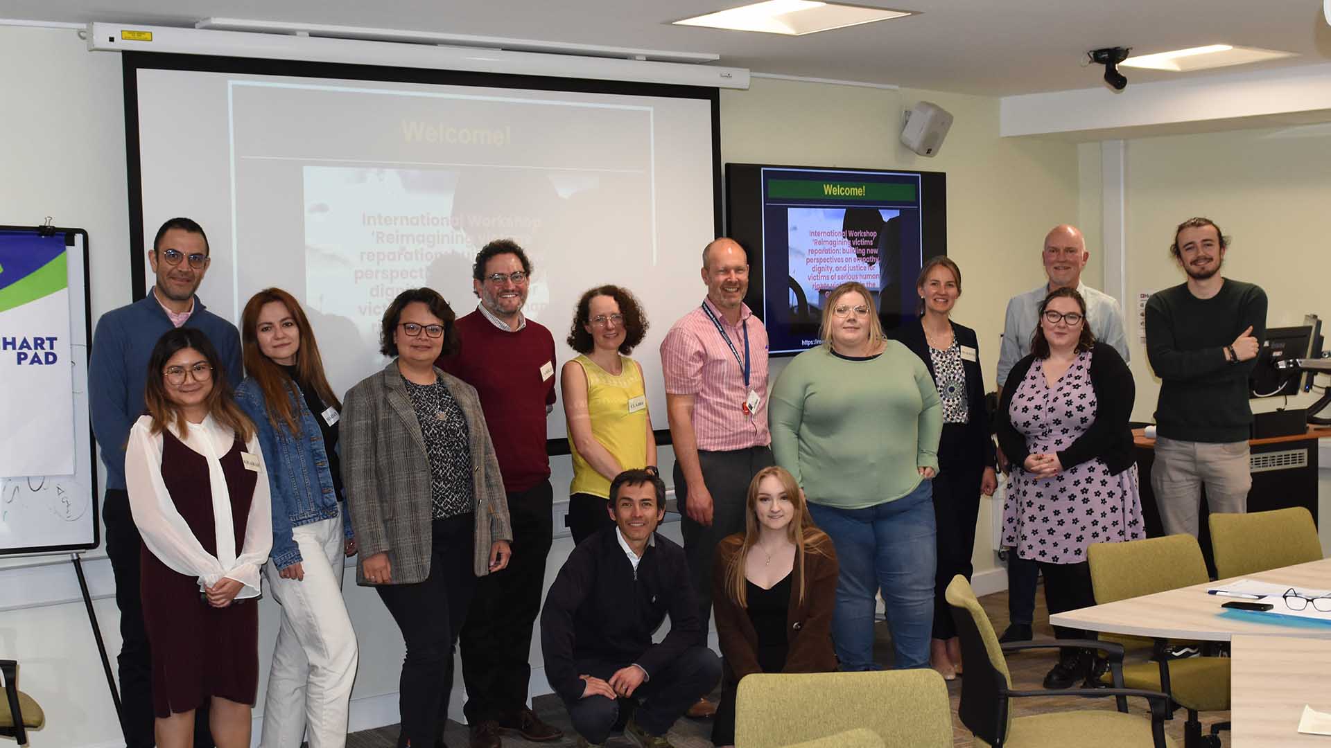 The group of academics who attended a workshop on human rights reparations stand in front of a screen