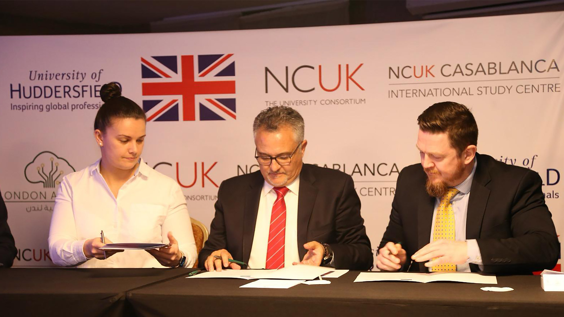 Three people sat at a table signing a document