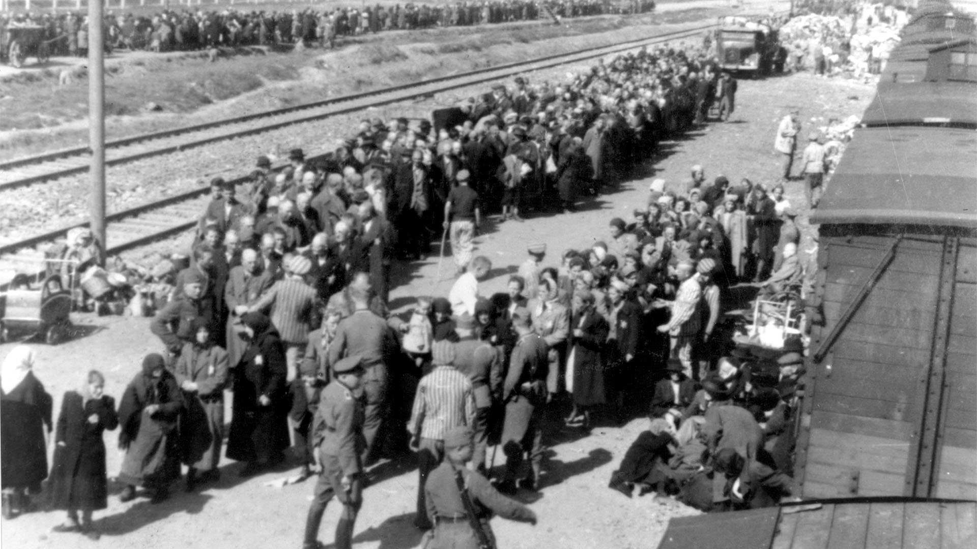 Victims of the Holocaust are herded off trains by Nazi officers at a death camp