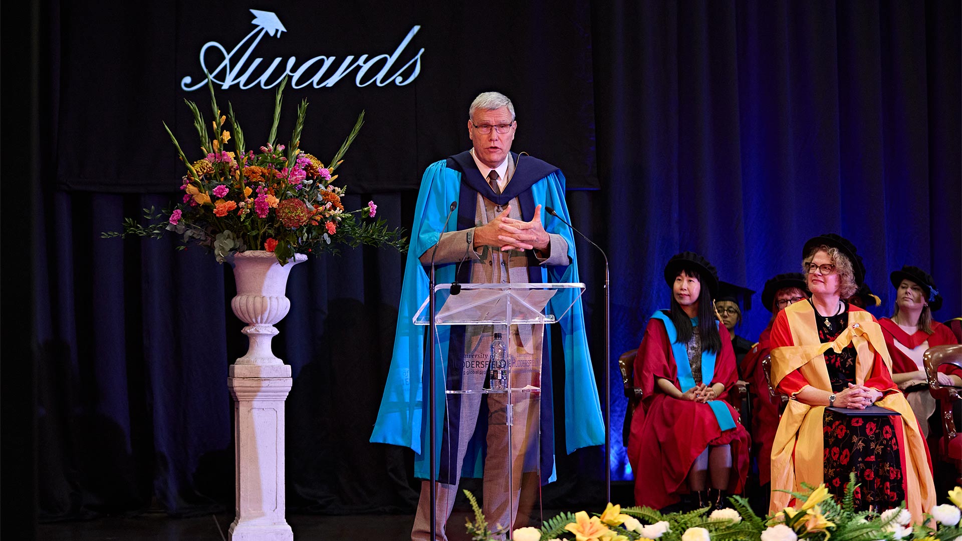 A man at a podium wearing a graduation gown