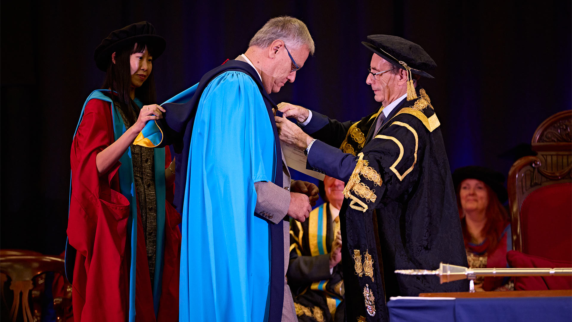 A man on stage at graduation being present with an award