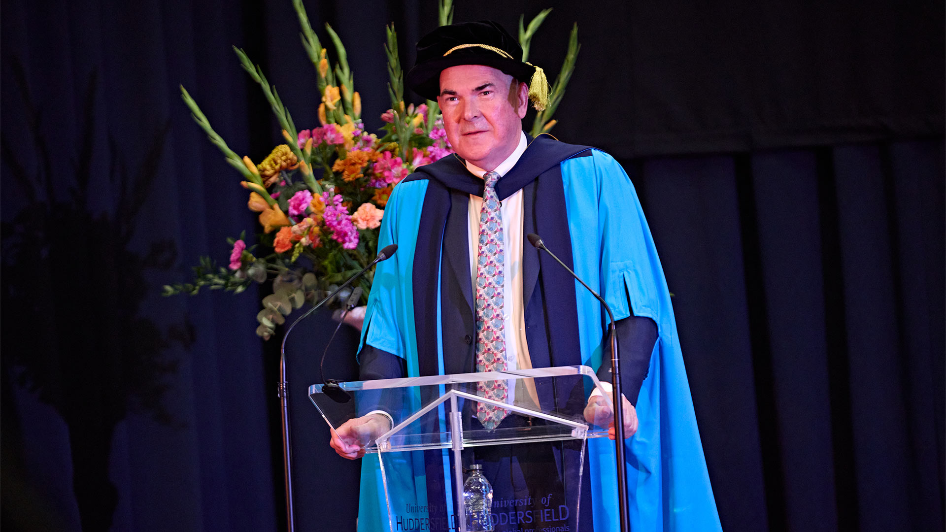 A man at a podium wearing a graduation gown