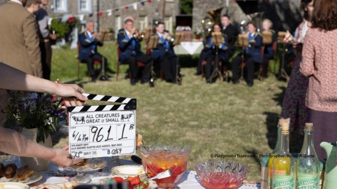 A clapperboard about to be snapped in a scene of a tv series being filmed in sunshine