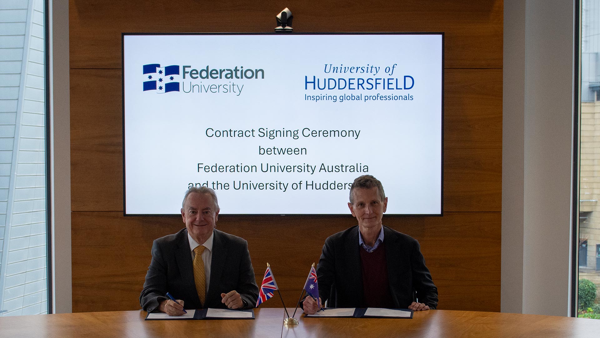 Two people sat behind a desk signing an official document