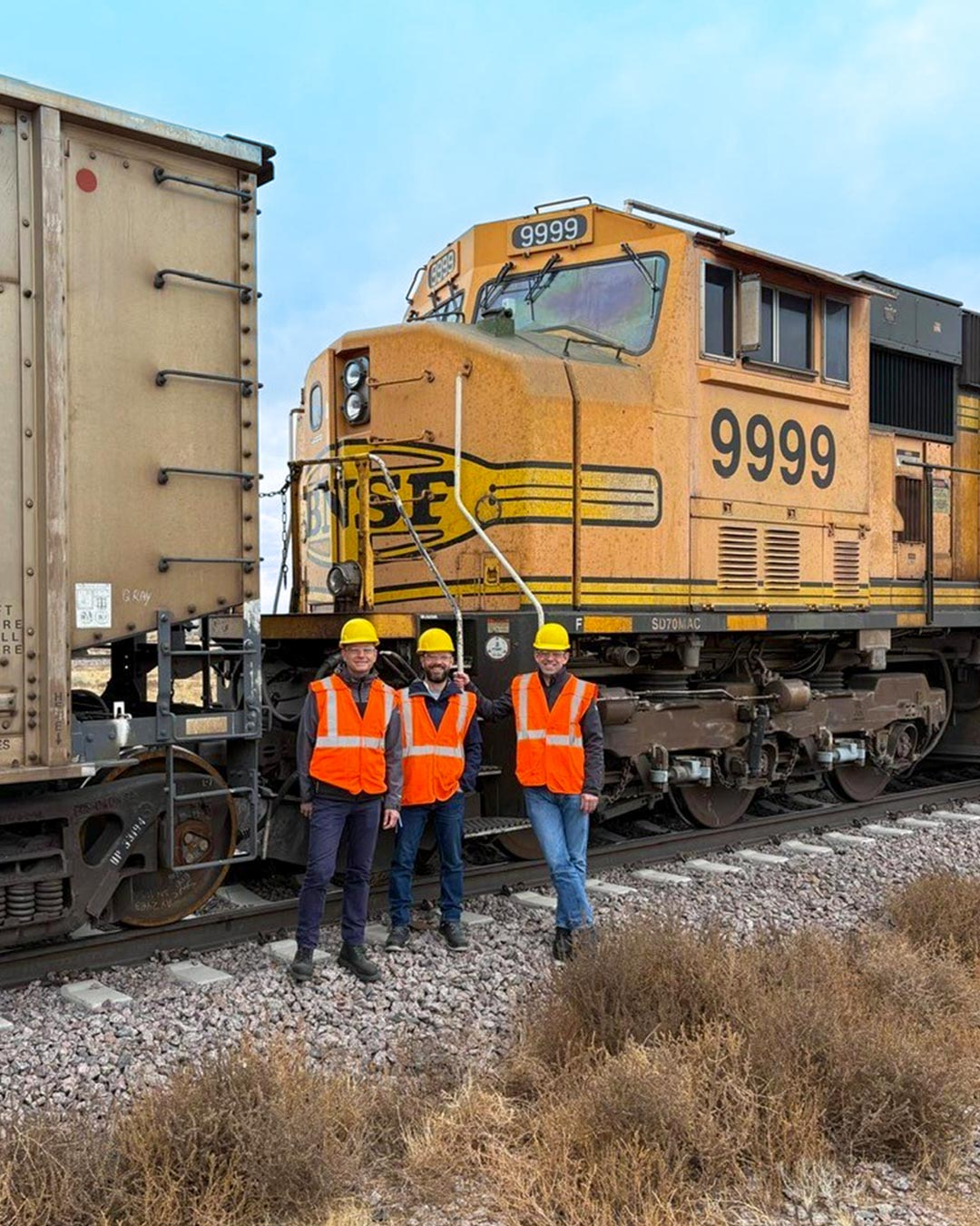 Three men in hi-vis jackets and hard hats stood infront of a train
