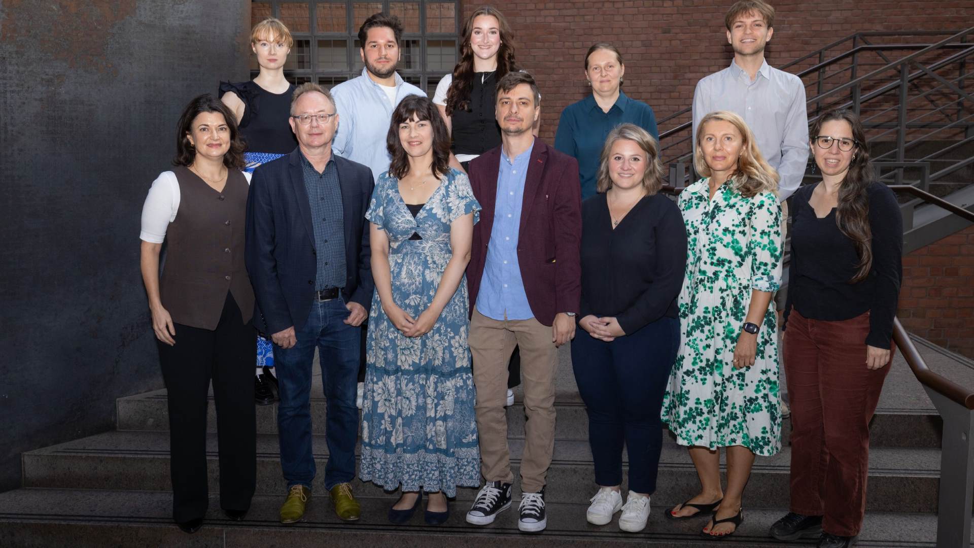A group of academics in two rows stand before the camera