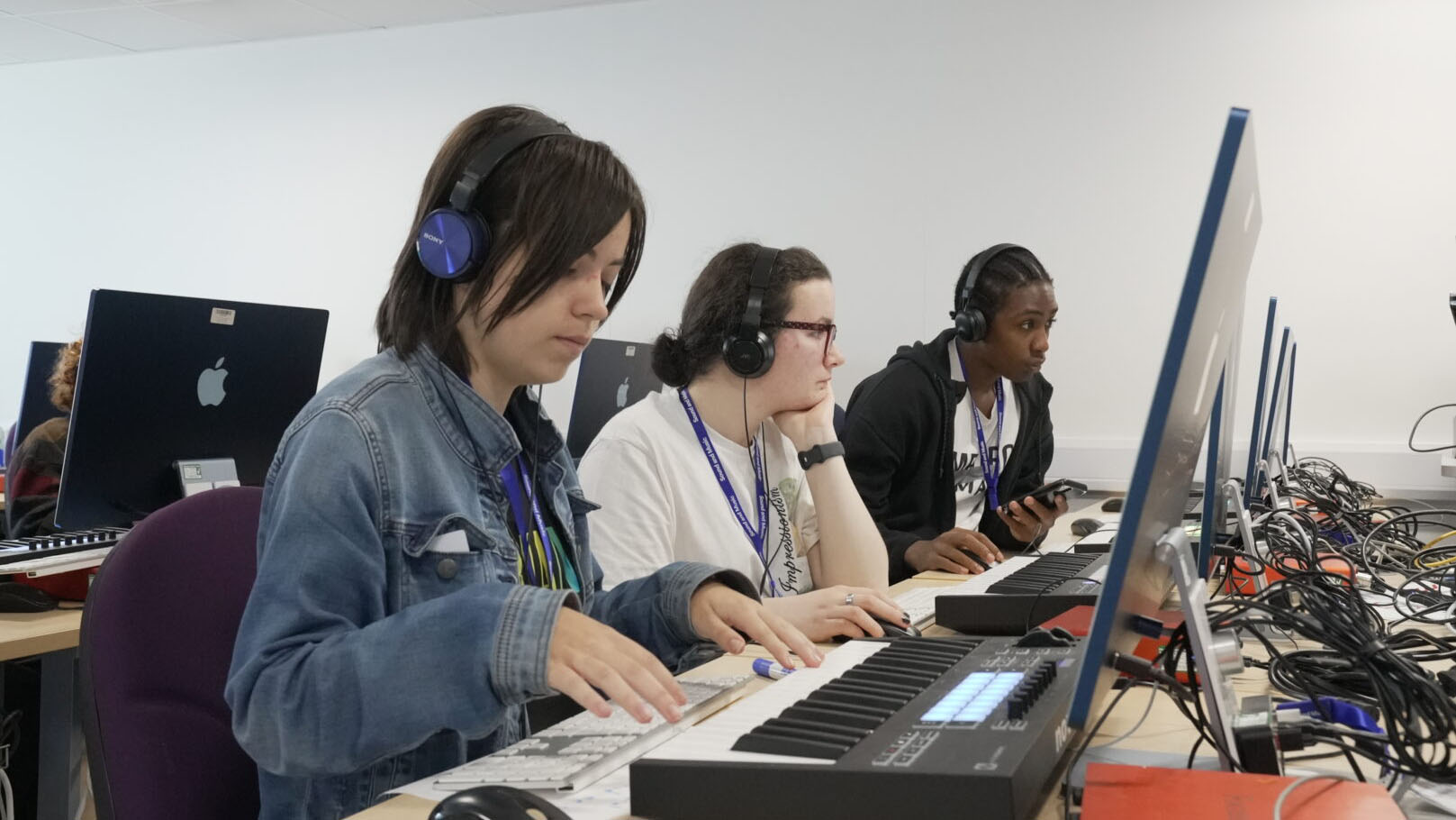 Young musicians look at screens with keyboards in front of them.
