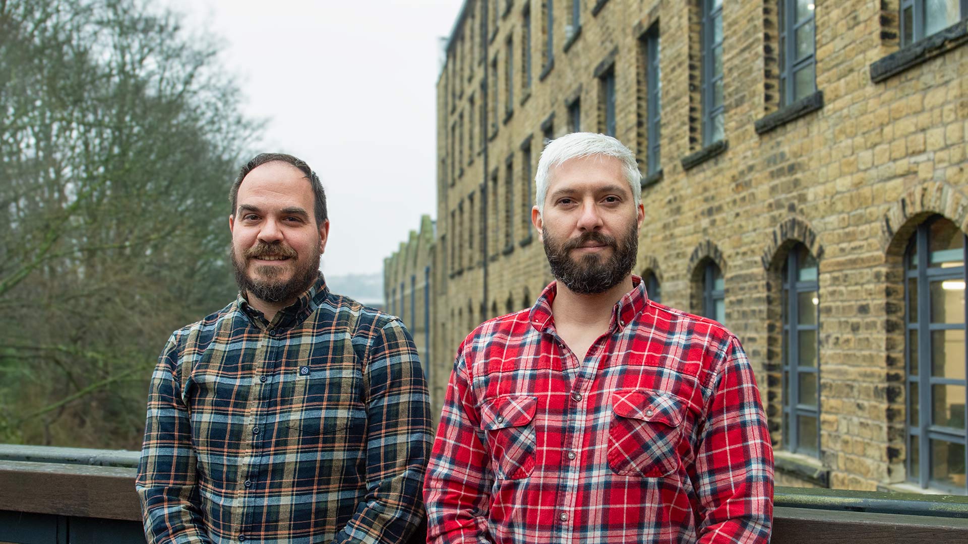 Two men stood on a bridge over a canal infront of a mill building