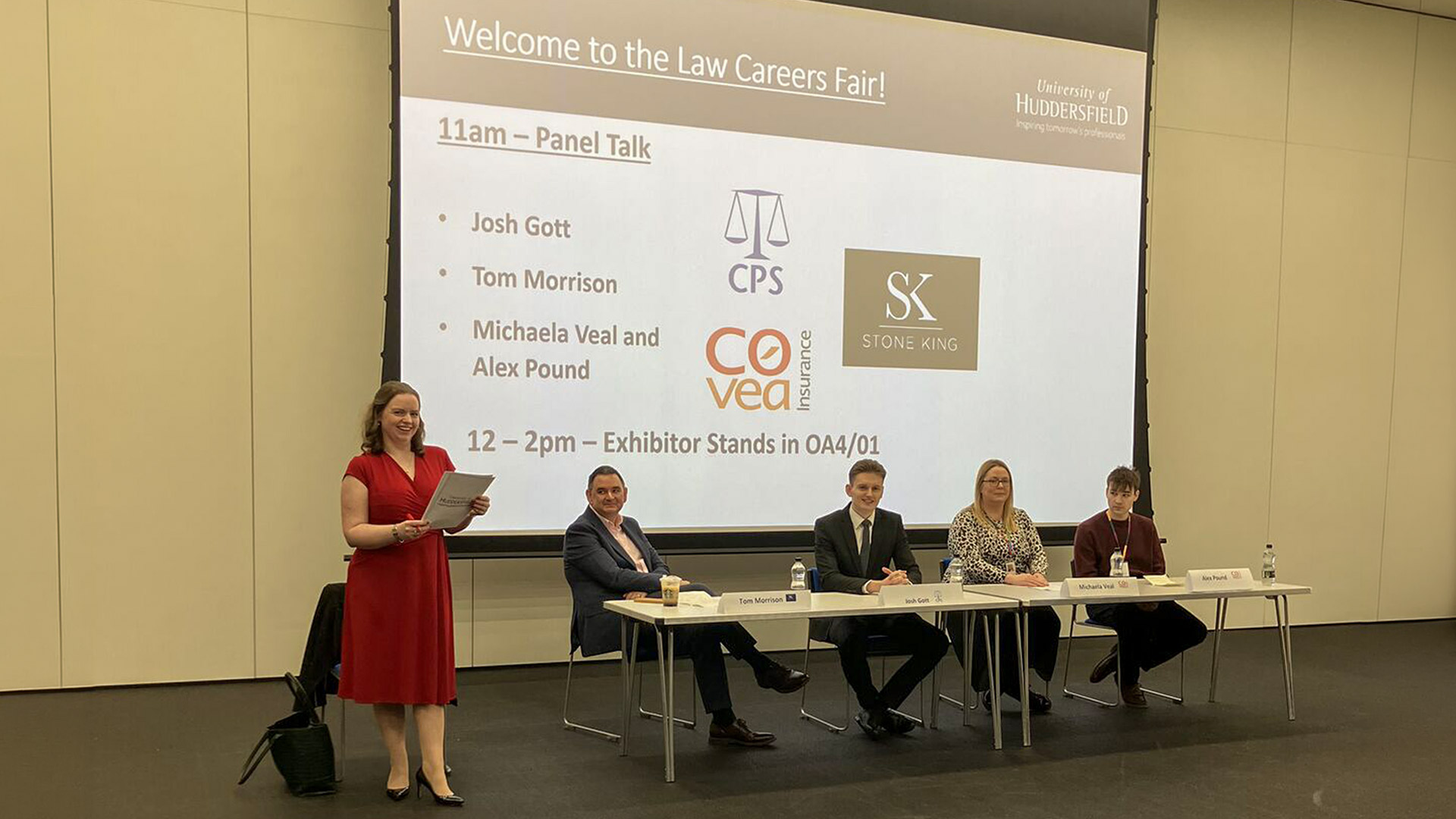 A lecturer standing at the front next to a panel of people during a question and answer session