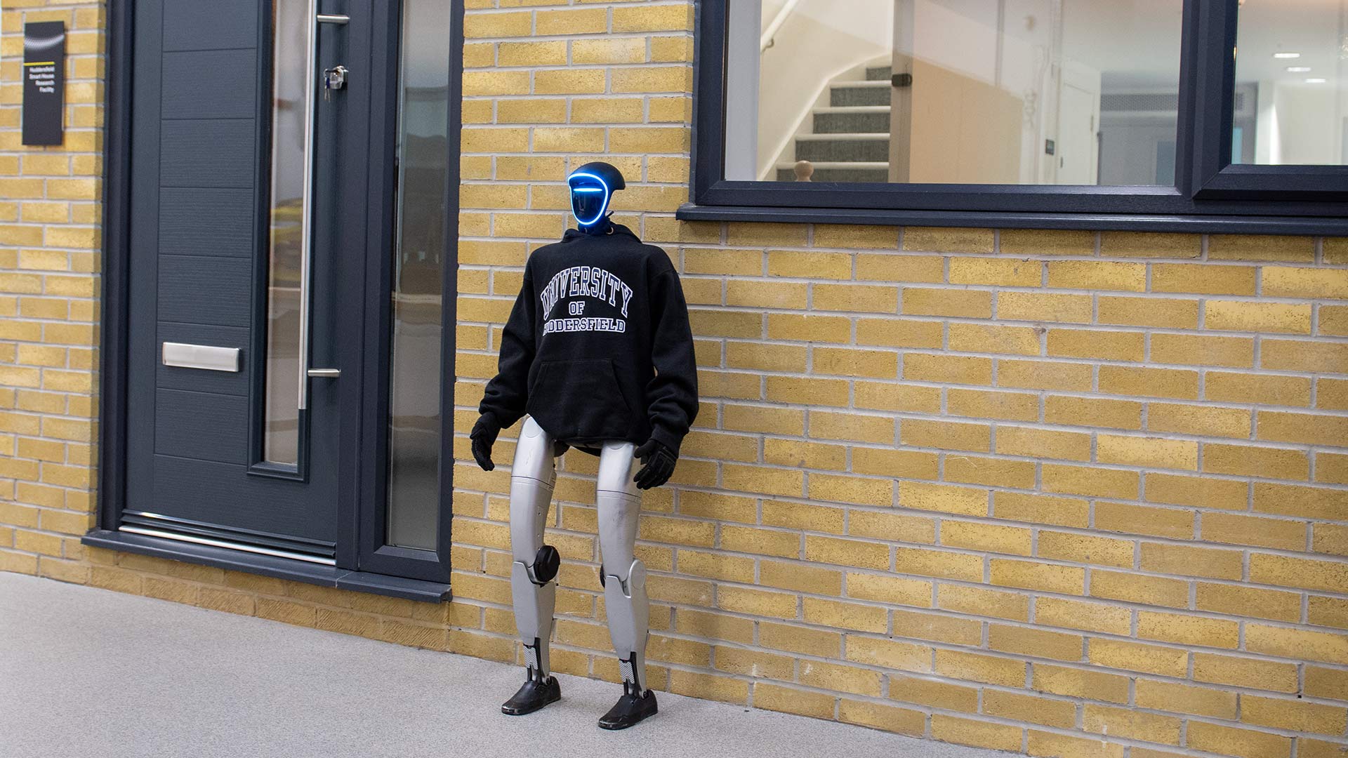A humanoid robot wearing a hoodie and standing outside of a house