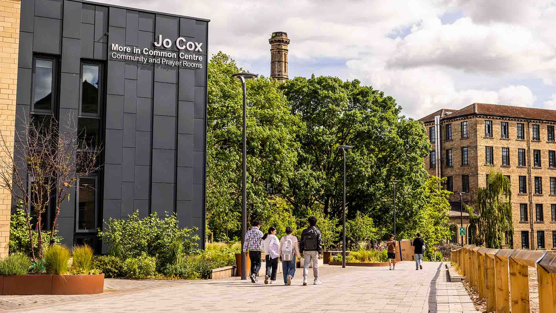 The Jo Cox More in Common Centre at the University of Huddersfield campus in sun with four students walking away from the camera