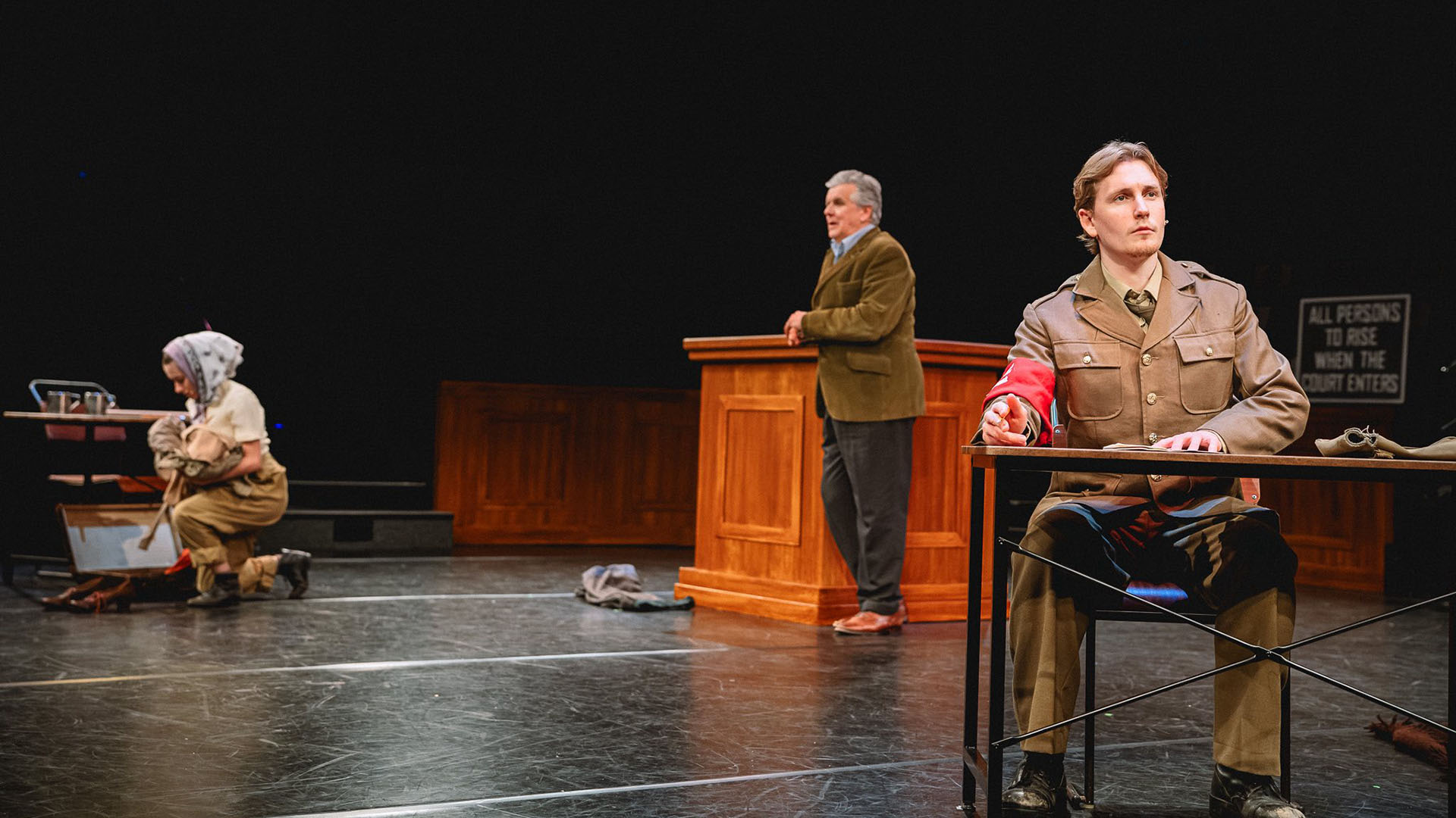 Three actors on stage in a Holocaust docudrama in a mock court room
