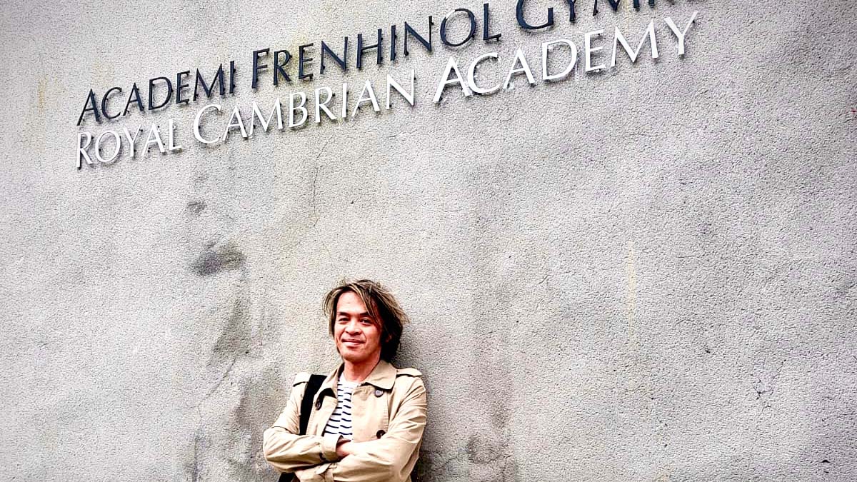 Frank To in front of a sign at the Cambrian Royal Academy