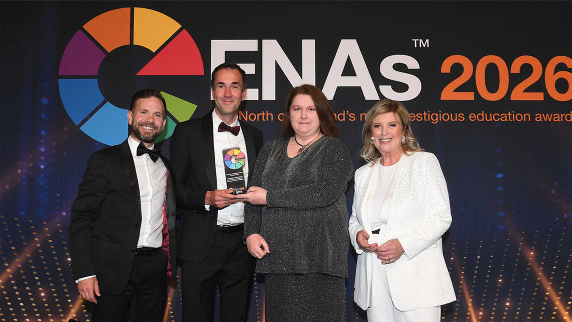 Four people in formalwear pose at the ENAs 2026, one holding a glass award trophy, standing on stage beneath prominent event logo and text.
