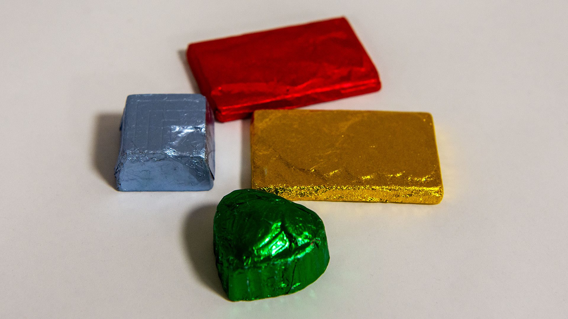 Close-up of colourful chocolate samples wrapped in foil in red, blue, yellow and green placed on a white surface.