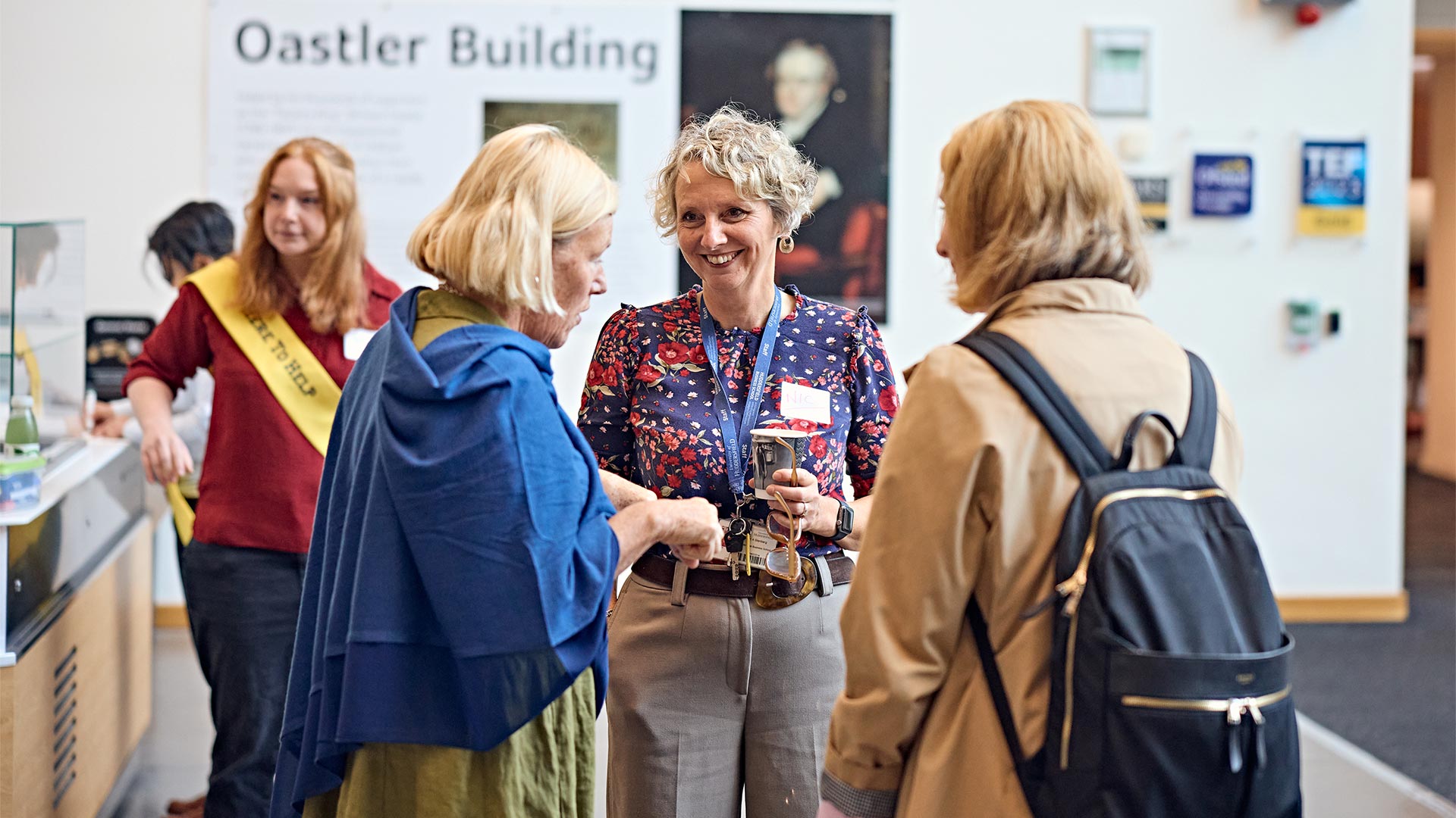 Attendees talk beside heritage displays during the Leading with Humanity in Health and Social Care event, held in a university exhibition space with interpretation panels and exhibits visible.
