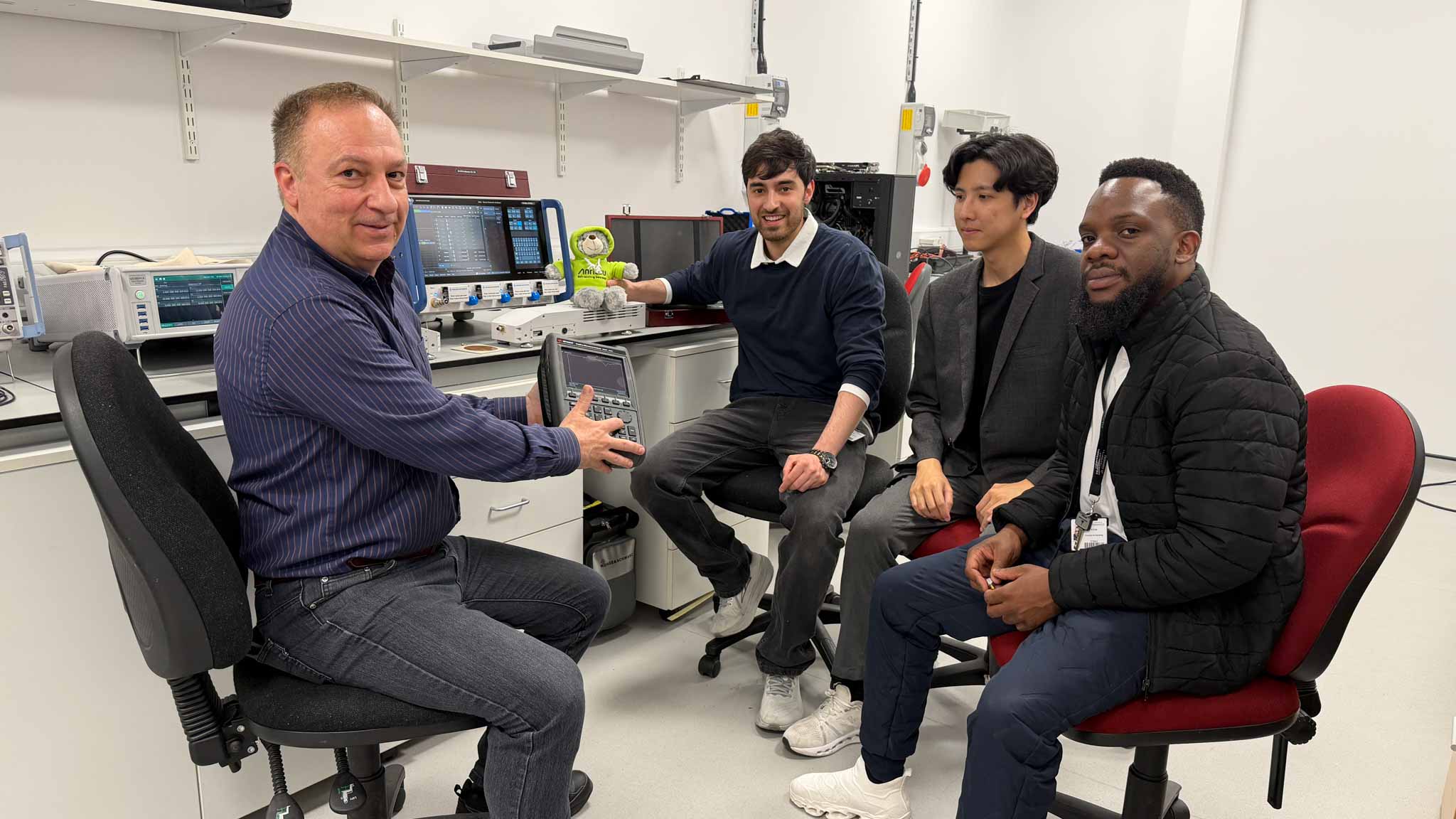 Students and research supervisor discussing project with supervisor presenting electronic engineering equipment