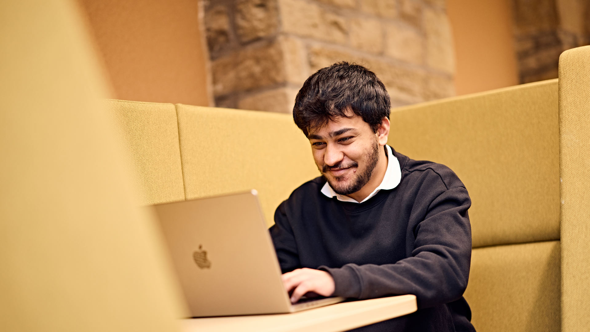 Postgraduate student working on laptop in study space on campus