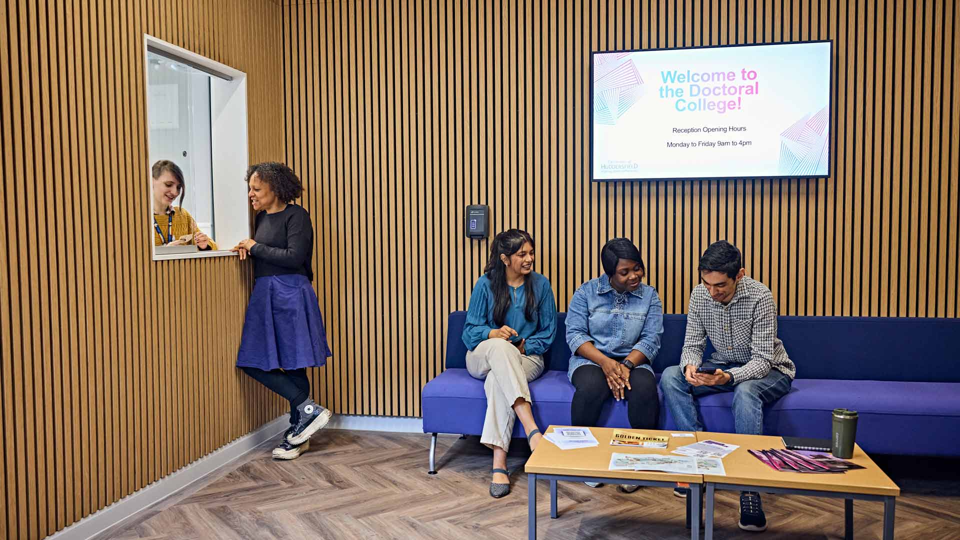 Students sitting in Doctoral College reception area and talking with staff from the College