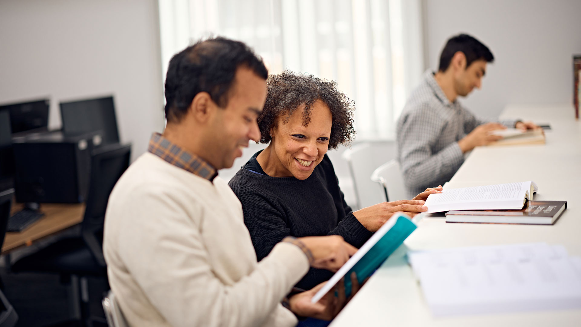 Postgraduate researchers smiling and discussing project work together in the Doctoral College building
