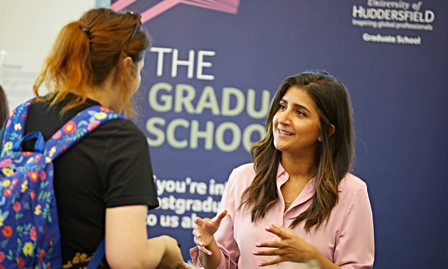 two people talking in front of a graduate school banner