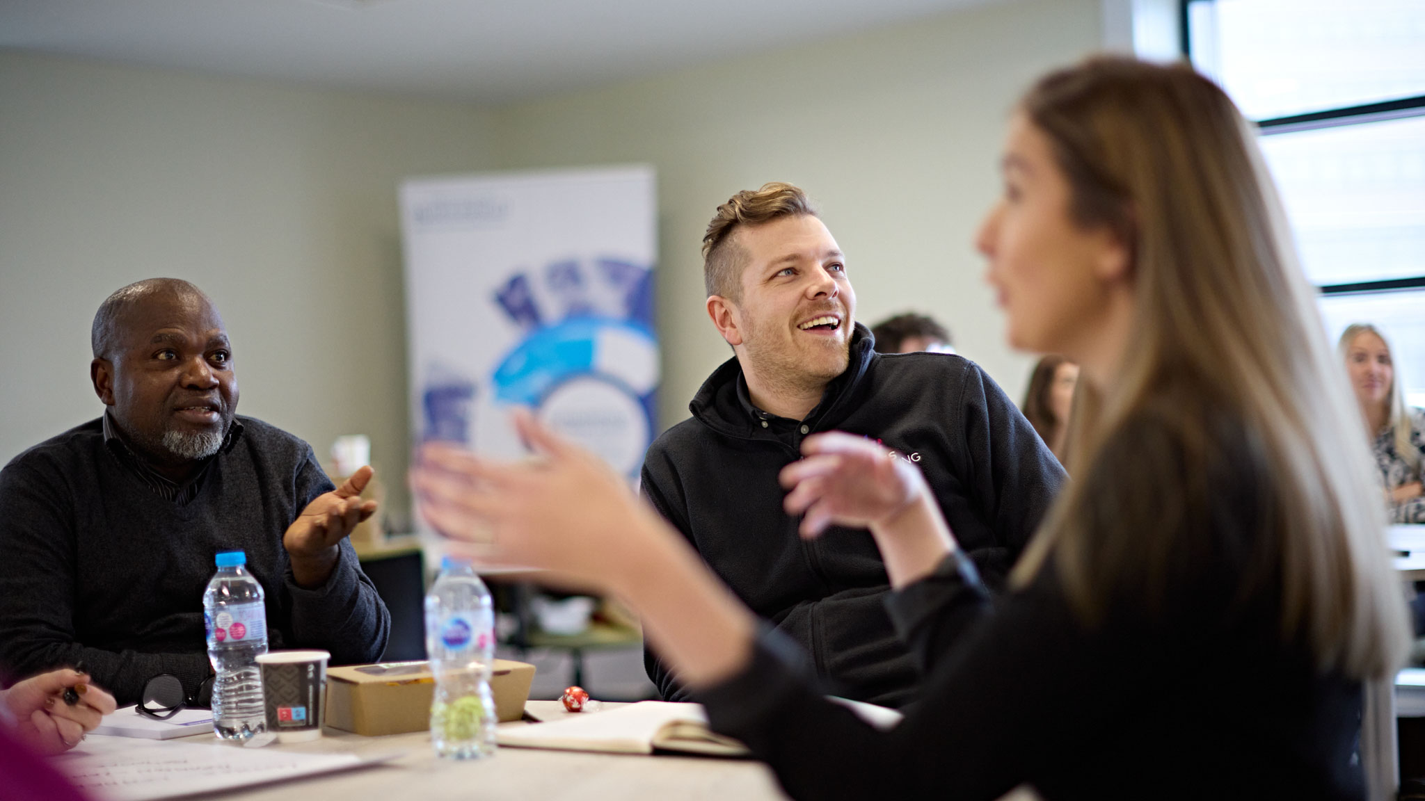 Three students chatting and laughing together around a table