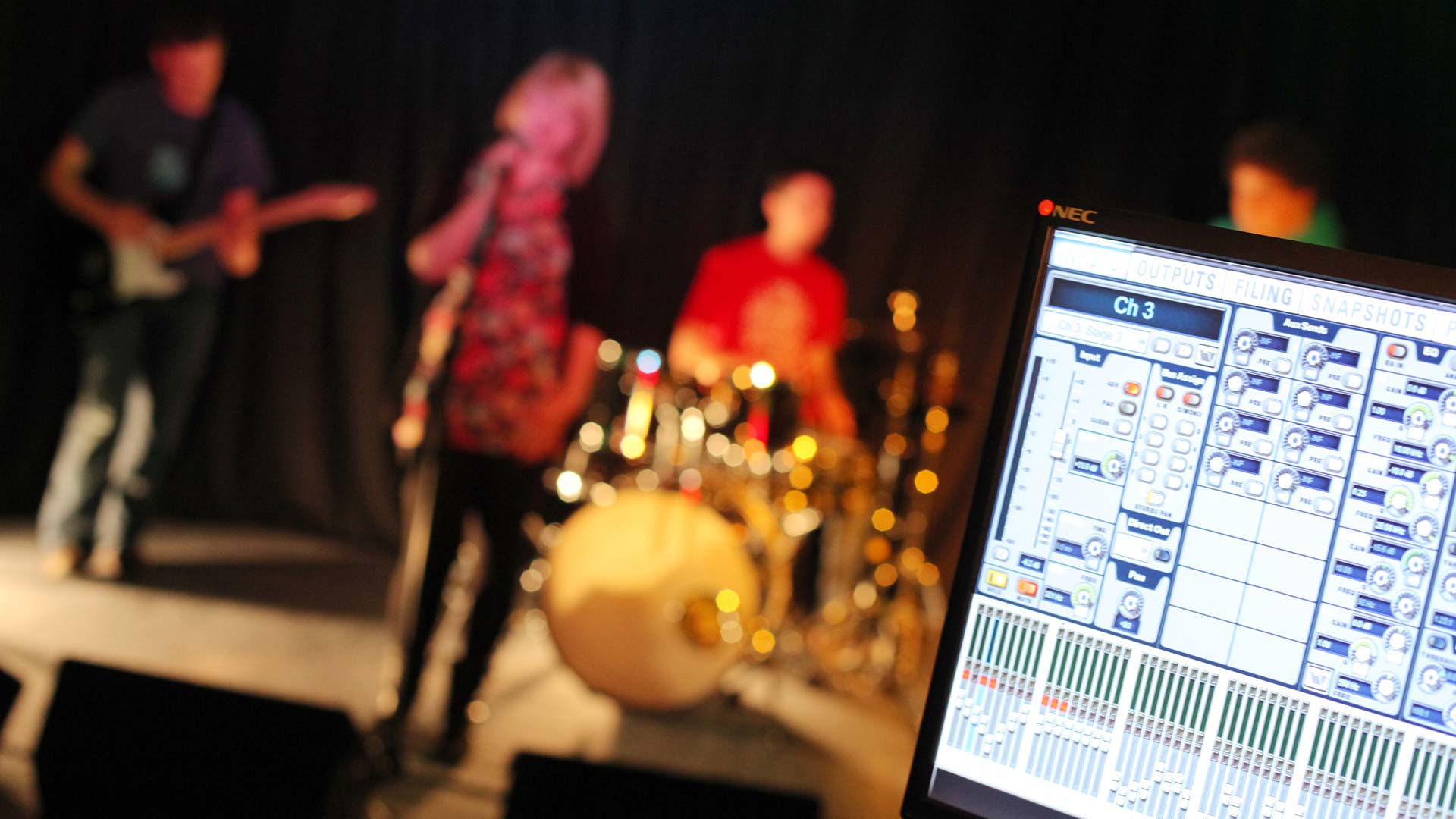 Blured band in the background with a monitor showing a soundboard software close up.